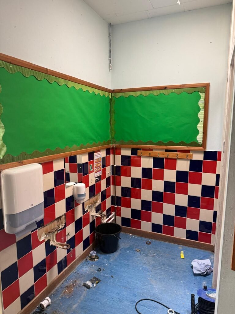 School washroom during strip out, with the old wall hung basins removed from red and blue tiled walls