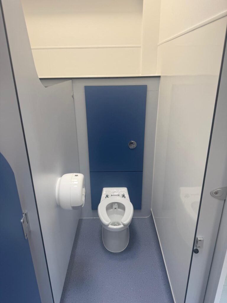 Inside a finished school toilet cubicle, with an infant height WC, concealed cistern behind a blue IPS panel and a toilet roll dispenser