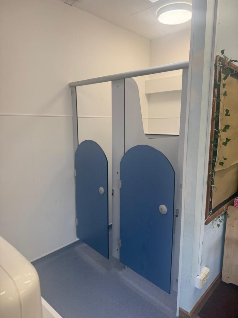 Finished school toilet cubicles with blue curved top doors, grey pilasters, white wall panelling and new safety vinyl flooring