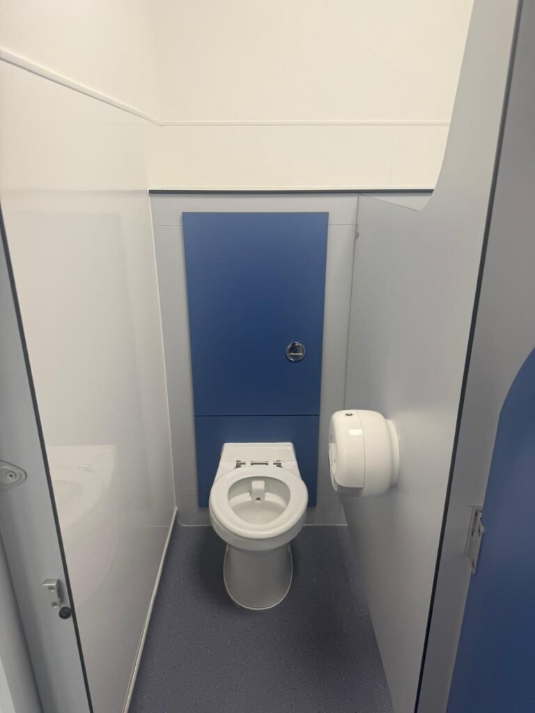 Finished school toilet cubicle with a back to wall WC pan, concealed cistern behind a blue IPS duct panel and white wall panelling