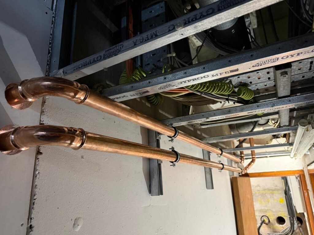 Two new copper water pipes run at high level along a wall at Free Trade Wharf